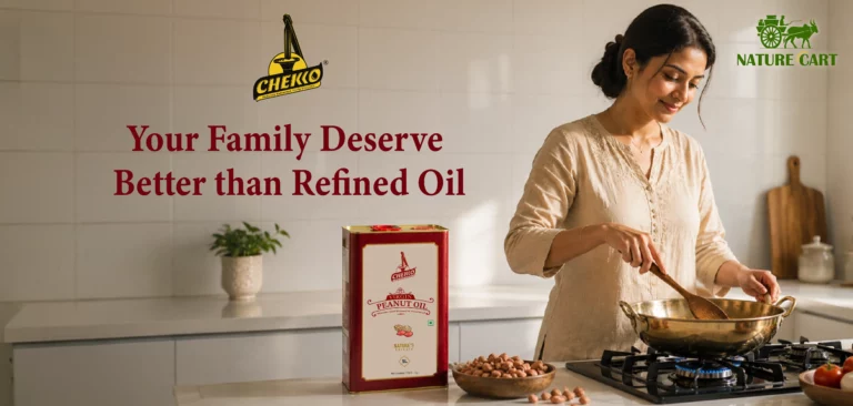 A premium lifestyle kitchen scene featuring a smiling South Asian woman cooking in a bright modern kitchen with white tiled walls. A CHEKKO 5L cold pressed peanut oil tin is placed on the countertop beside raw peanuts, while warm natural sunlight fills the elegant kitchen space, creating a clean, authentic, and healthy cooking atmosphere.